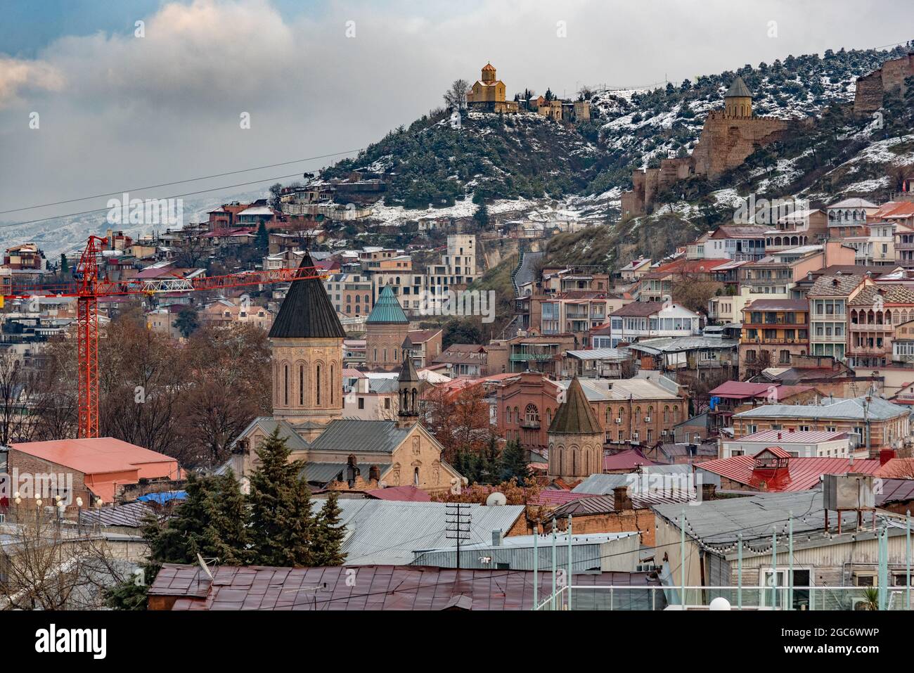 Roof-top view over the old town of Tiblisi, Georgia's capital city, in late winter, with dusting of snow on roofs and hillsides and dramatic sky Stock Photo