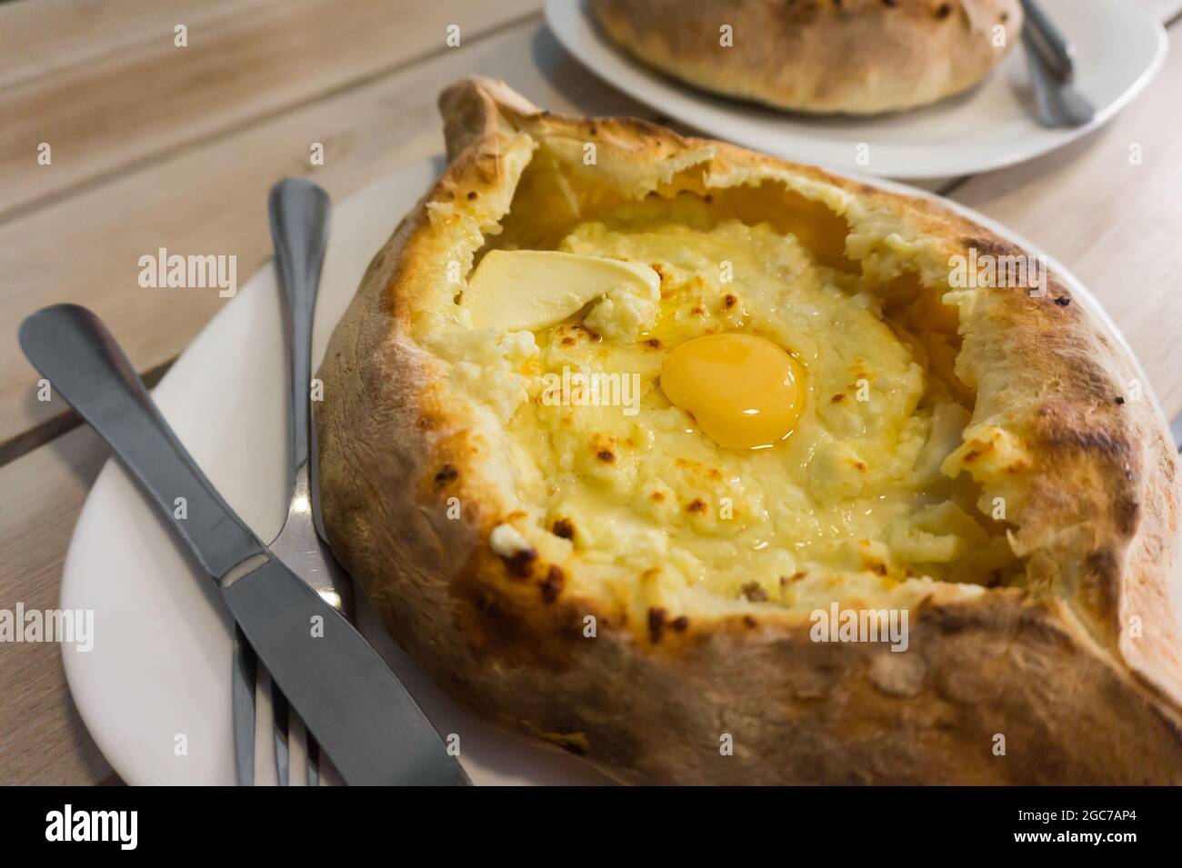 Khachapuri traditional Georgian Adjara cuisine meal on a plate in a restaurant. Baked bread with cheese and egg filling close-up Stock Photo