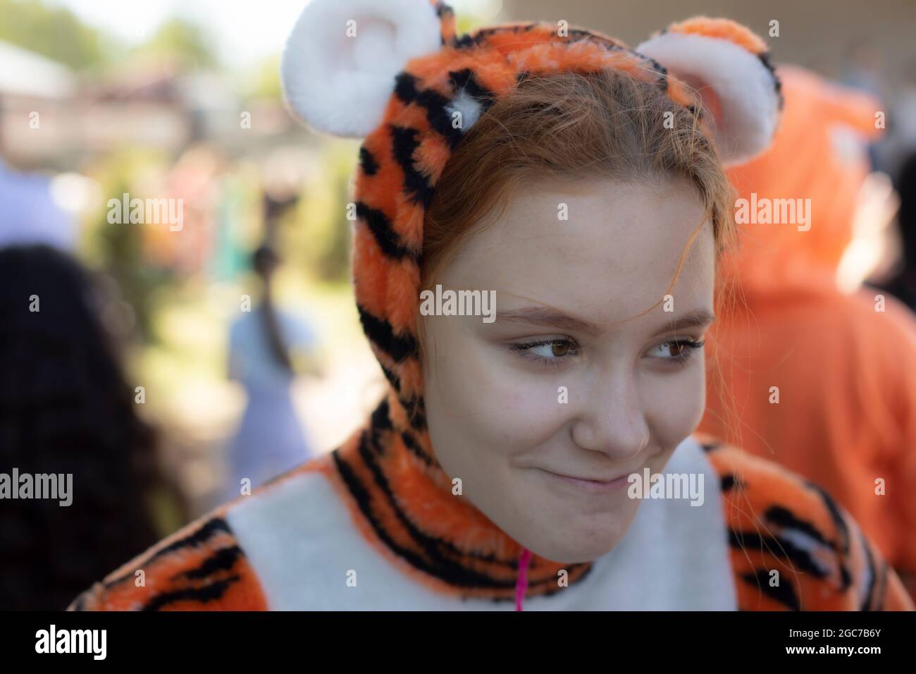 A girl dressed as a tiger. Children's animotr in a soft costume of a wild cat. A cute girl with red hair dressed in a cheerful outfit. Stock Photo