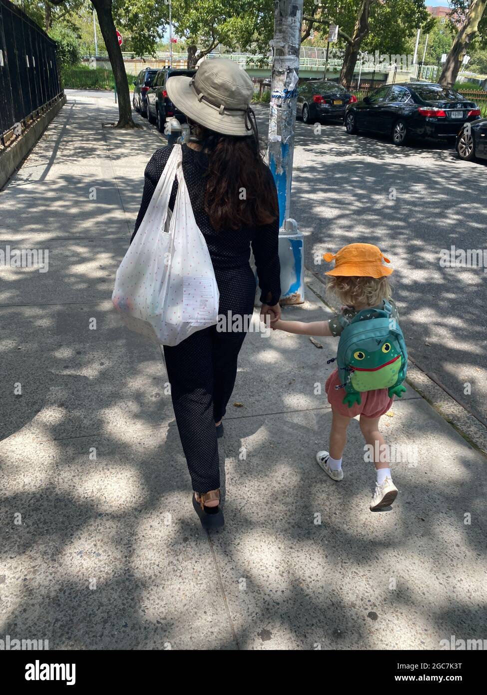 Mother and daughter wearing summer hats walk hand in hand on a quiet street in the Windsor Terrace neighborhood of Brooklyn, New York. Stock Photo