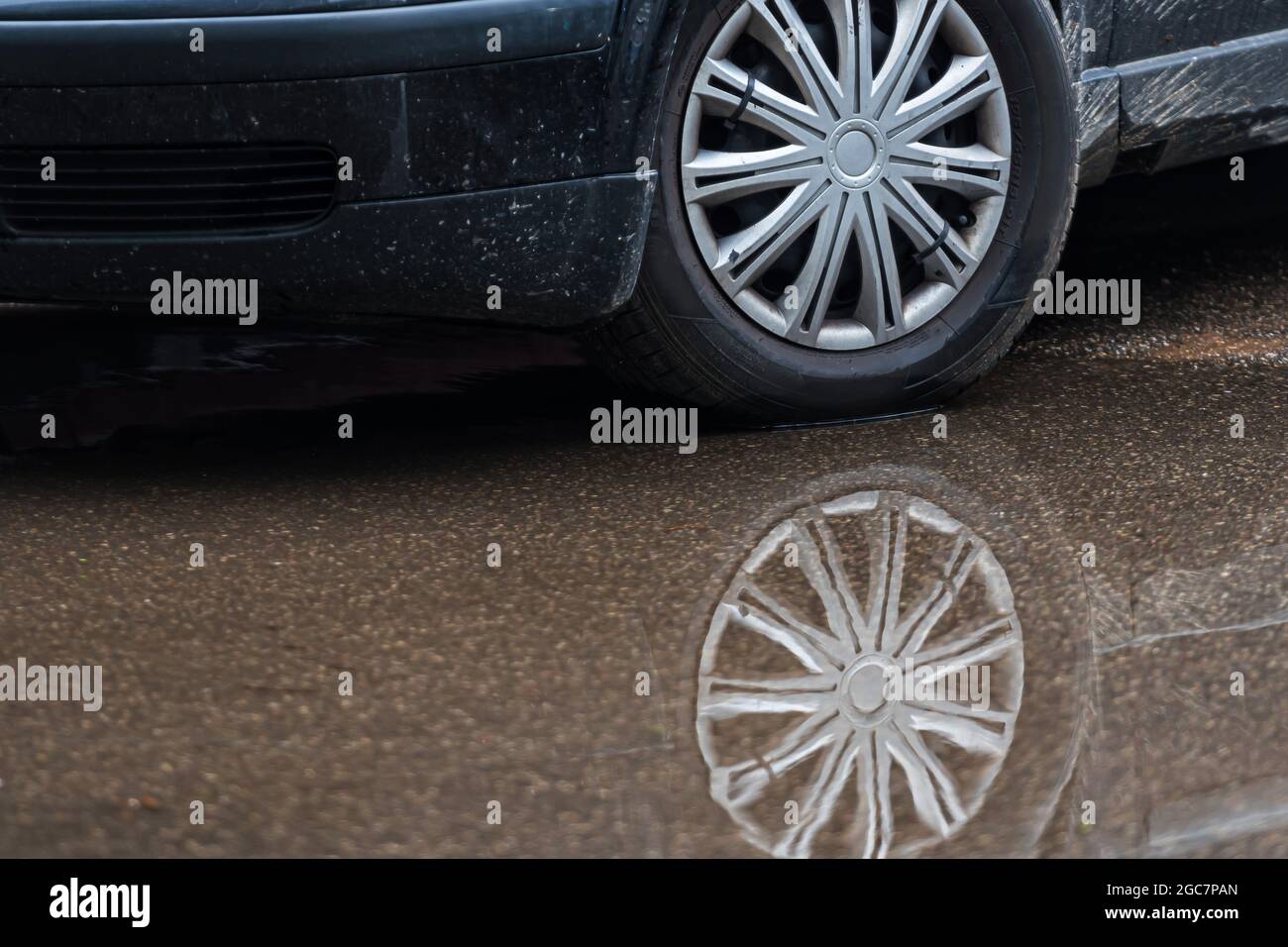 puddle on the pavement with a reflection of the car wheel, closeup
