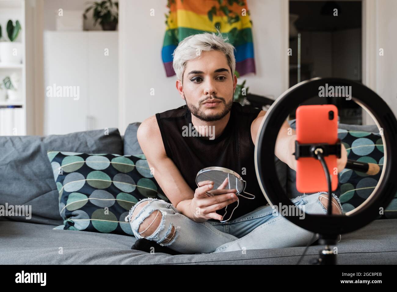 Gay man streaming online make up video tutorial with mobile phone indoors at home - Lgbt, drag queen, technology trendy concept - Focus in face Stock Photo