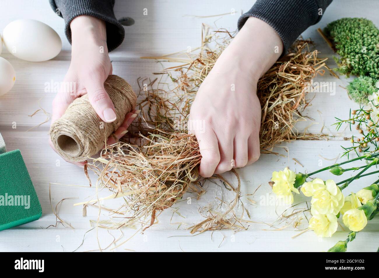 Florist at work: How to make Easter table centerpiece with carnations, wax flower, eggs and moss. Step by step, tutorial. Stock Photo