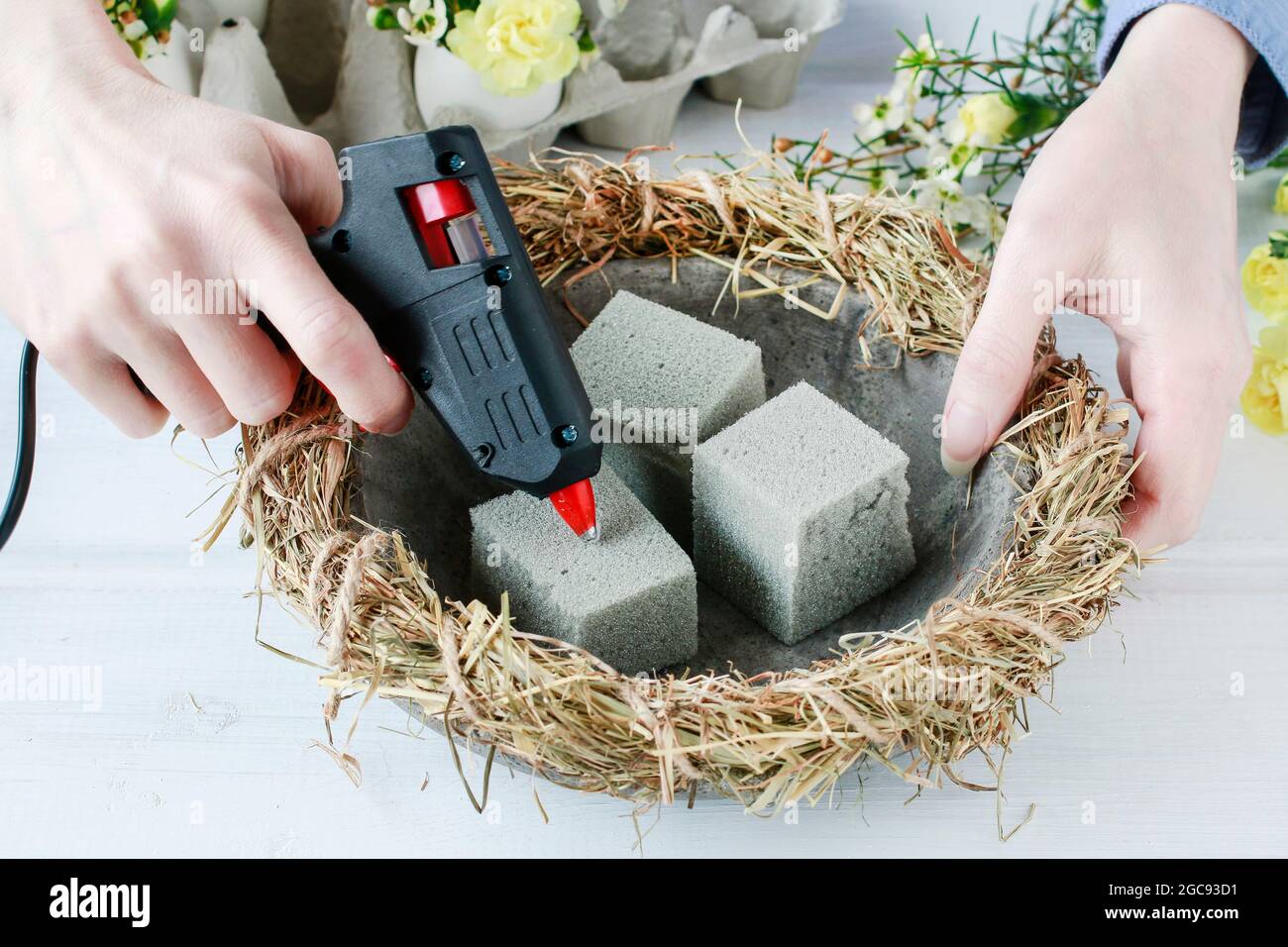 Florist at work: How to make Easter table centerpiece with carnations, wax flower, eggs and moss. Step by step, tutorial. Stock Photo