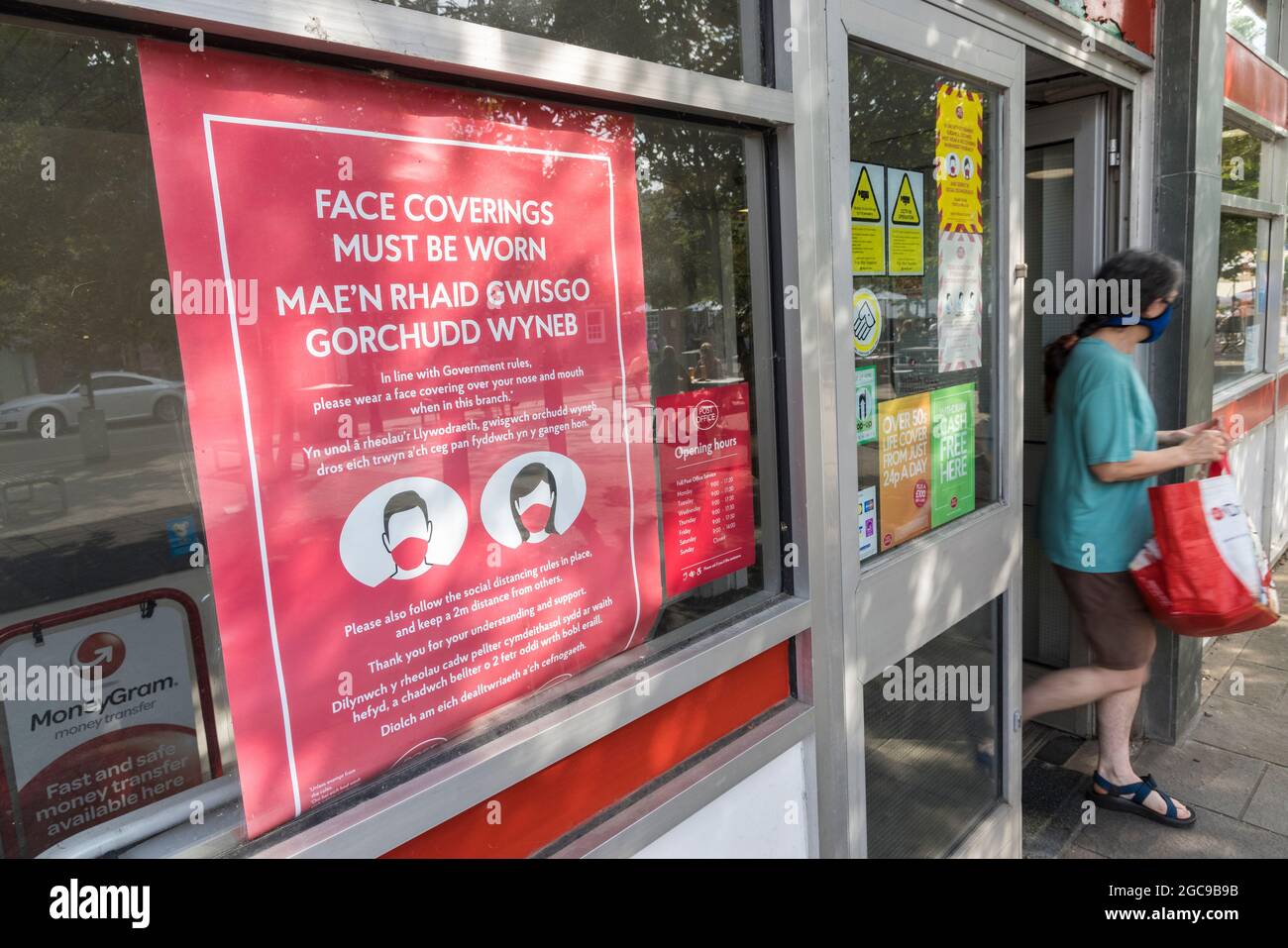 Face coverings must be worn sign on Post Office with person walking out, Abergavenny, Wales, UK