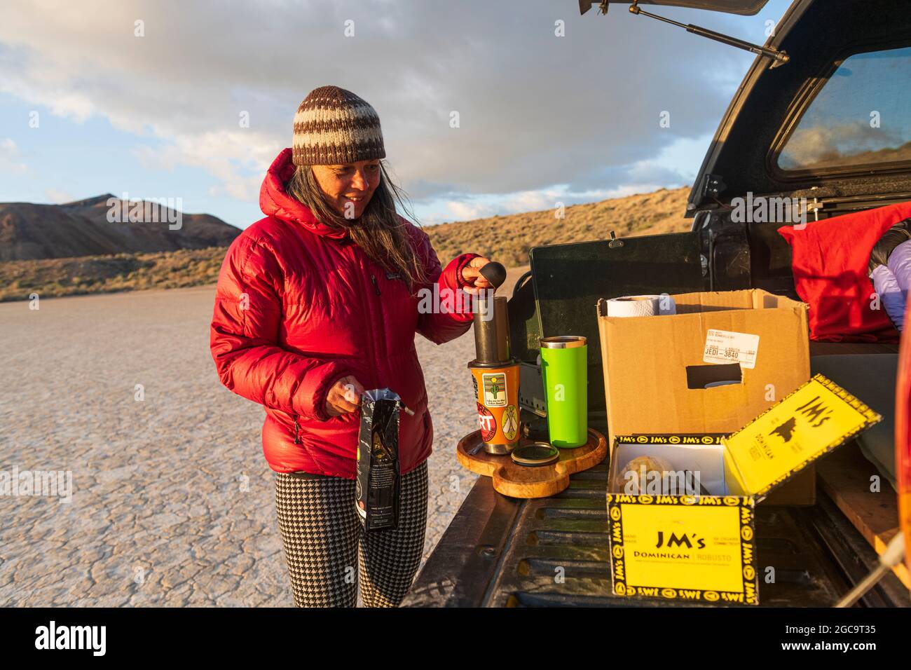 Woman makes coffee at sunrise camping on the playa in the Black Rock Desert, Nevada with the granite mountain wilderness in the background Stock Photo