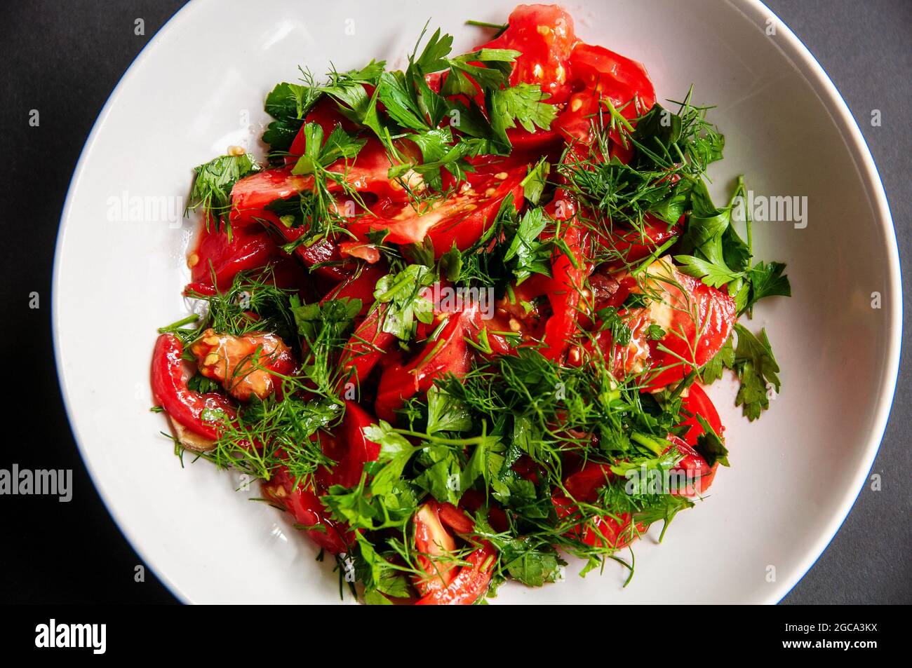 Parsley tomato and dill salad on a white plate. Healthy food for weight loss, vegetarian food. Fresh vegetables cut in a dish. Stock Photo
