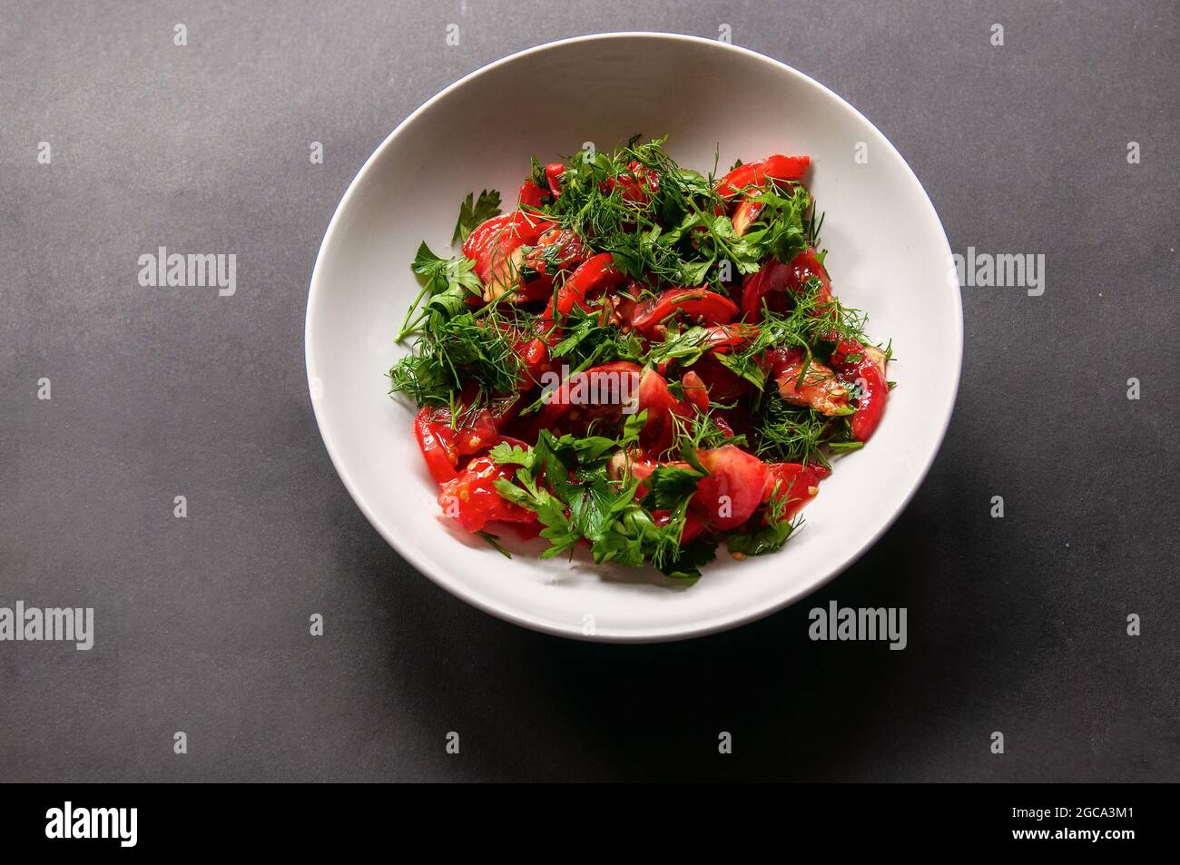Parsley tomato and dill salad on a white plate on a dark background. Healthy food for weight loss, vegetarian food. Fresh vegetables cut in a dish on Stock Photo