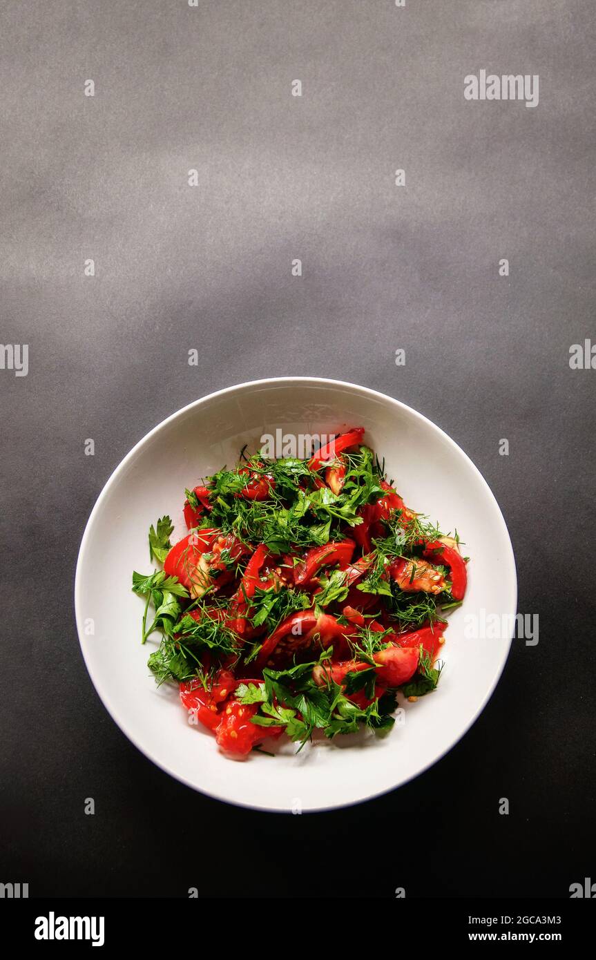 Parsley tomato and dill salad on a white plate on a dark background. Healthy food for weight loss, vegetarian food. Fresh vegetables cut in a dish on Stock Photo