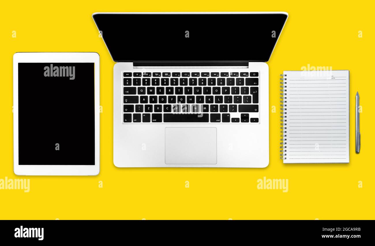 Computer, tablet and notebook on a solid yellow background. Minimalistic flat lay composition. Stock Photo