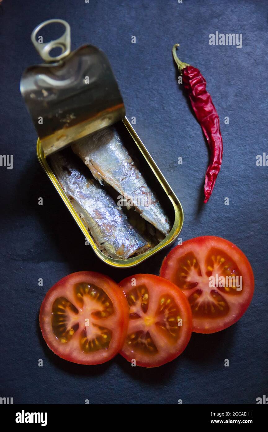 Closeup of a can of sardines next to some red tomatoes and a chilli on a black slate Stock Photo