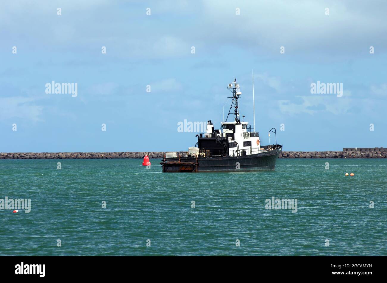 Small vessel in black and white heads toward the breakwater on Hilo Bay.  Blue sky and smooth sailing. Stock Photo