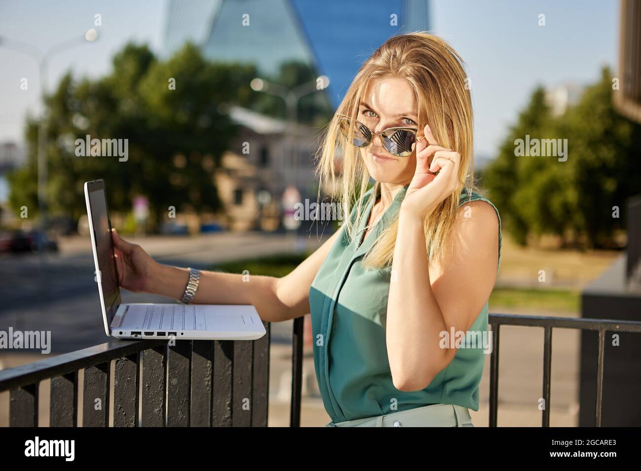 Woman with laptop outdoors works using internet in sunglasses. Stock Photo