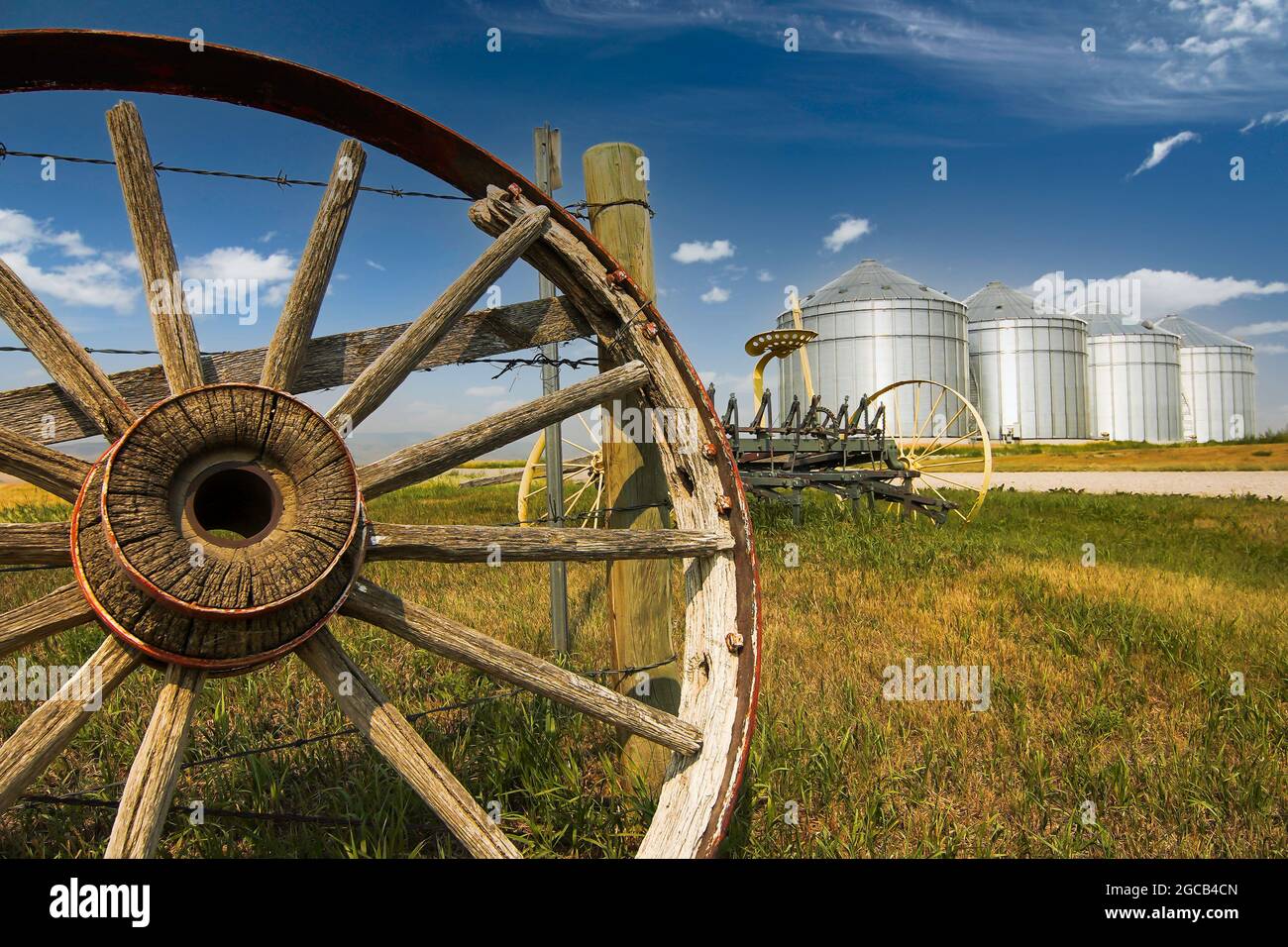 A vintage horse drawn cart wheel and grain silos on the Canadian Prairies during a summer day. Stock Photo