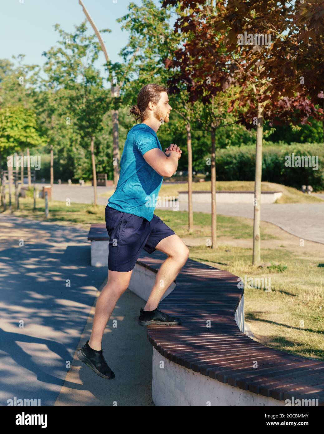 Young athletic guy in sports clothes doing exercising outdoors on sunny ...