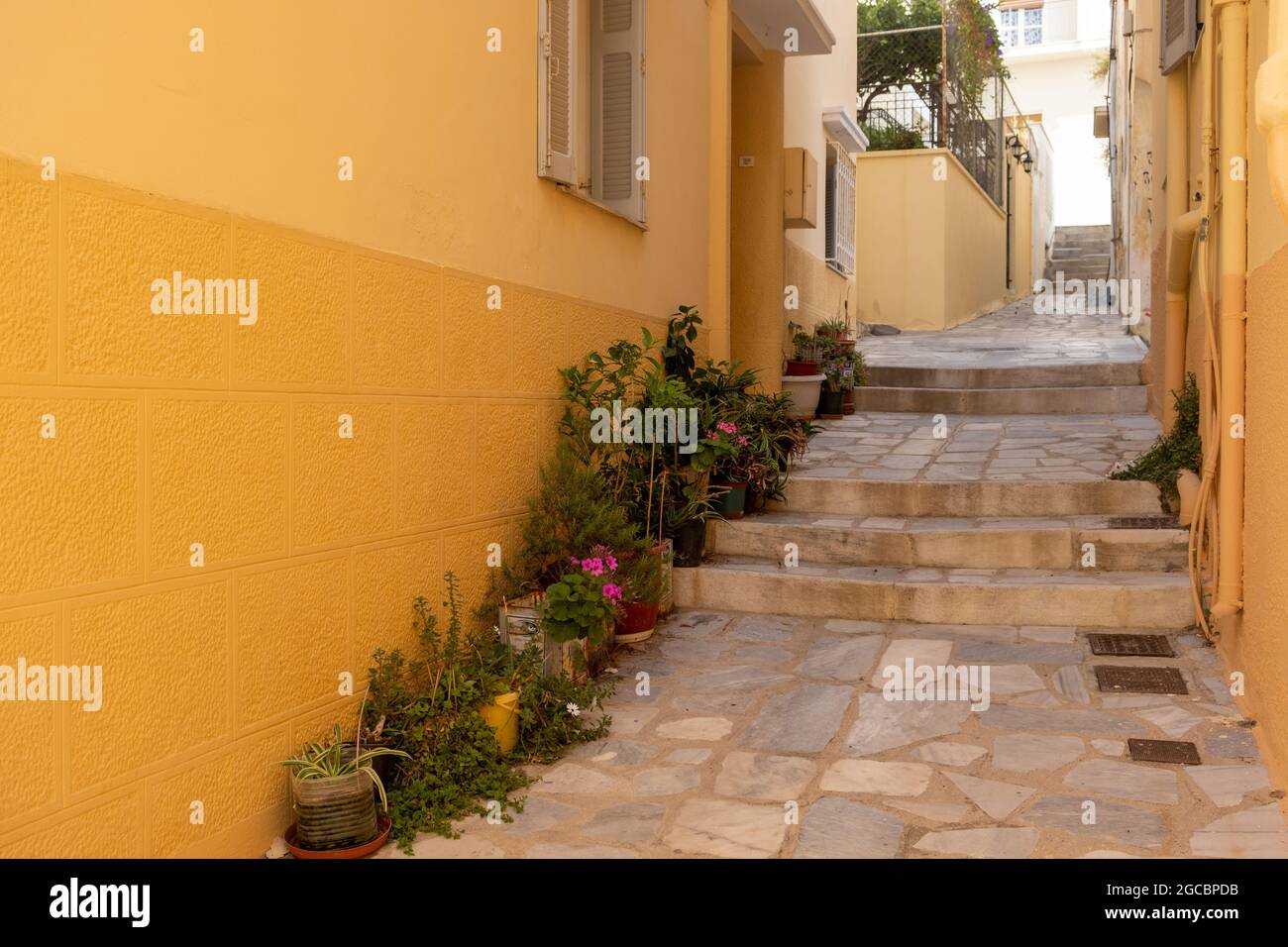 Traditional Greek island architecture. Empty cobblestone narrow alley with stone stairs between houses with orange stonewall summer sunny day. Destina Stock Photo