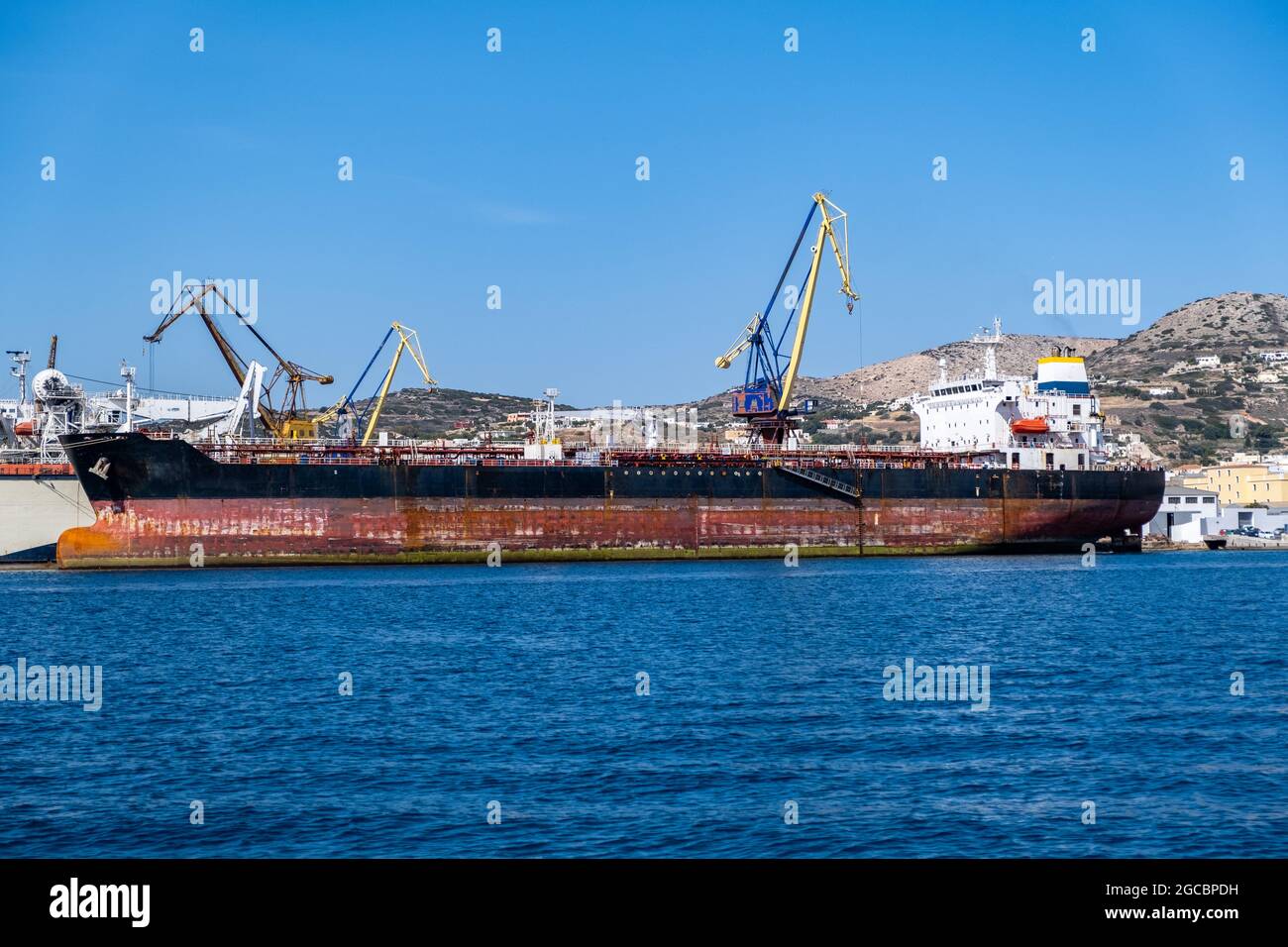 Syros island, capital Ermoupolis Cyclades Greece. Ships with cranes at Neorion shipyard harbor and industrial plant at Mediterranean sea. Dockyard int Stock Photo