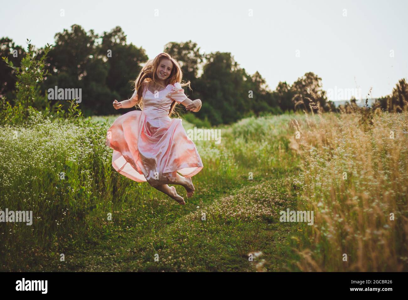 girl jumping in the field in a pink dress Stock Photo - Alamy