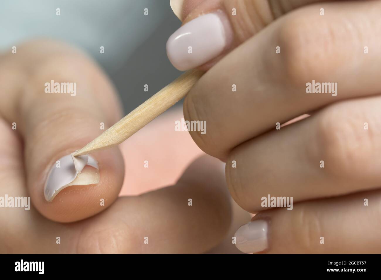 Remove the gel polish with a wooden stick. Woman is removing gel polish