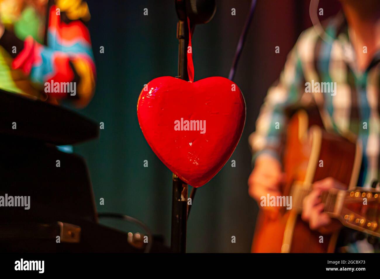 A heart as decoration on a microphone stand on a concert stage with blurred musicians in the background Stock Photo