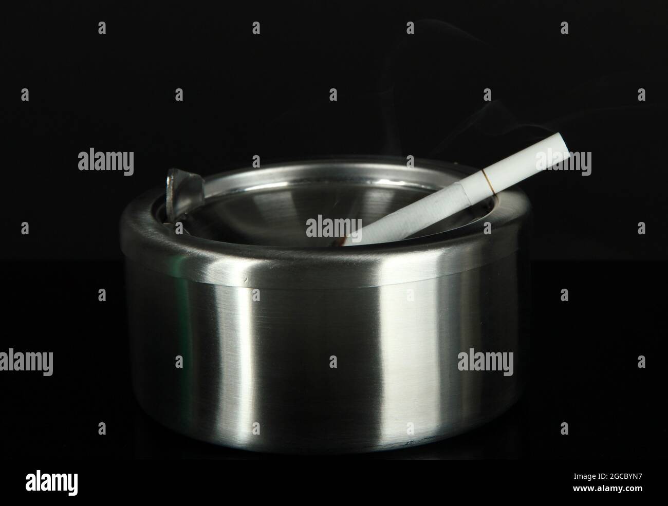 Metal ashtray and cigarette on black background Stock Photo - Alamy