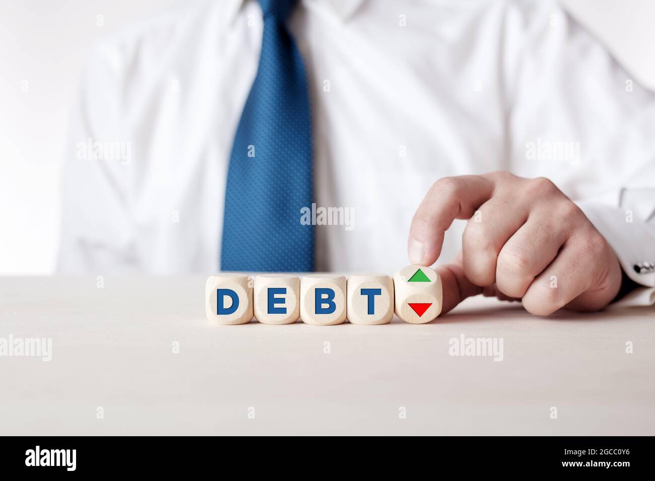 Businessman hand turns a wooden cube with arrows symbolizing the financial debt is rising or decreasing. Financial balance concept. Stock Photo