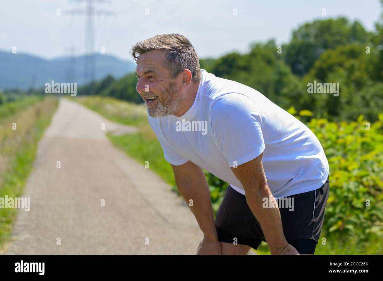 Middle-aged man pausing for a break to catch his breath while out jogging along a rural footpath on a lovely sunny day in a health and fitness and act Stock Photo