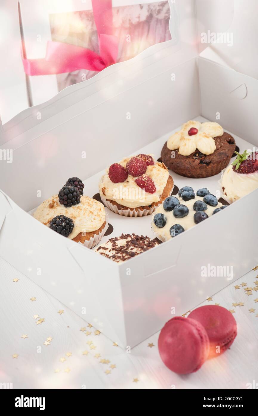 Cupcakes in a paper box with macarones. Pastel party or birthday composition with bokeh Stock Photo