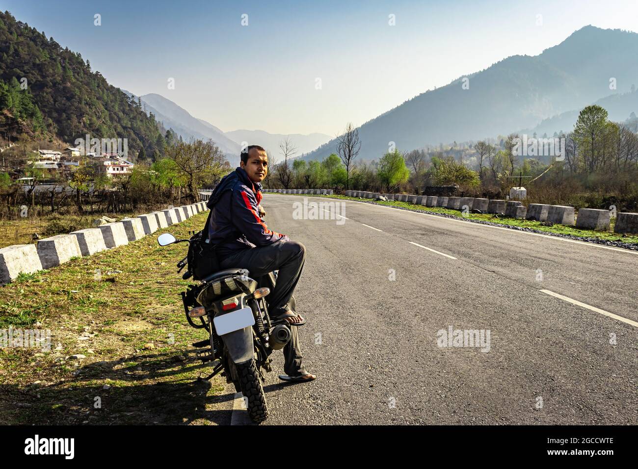 man sitting at motorcycle at tarmac road with beautiful natural view at morning image is taken at shergaon arunachal pradesh india. Stock Photo