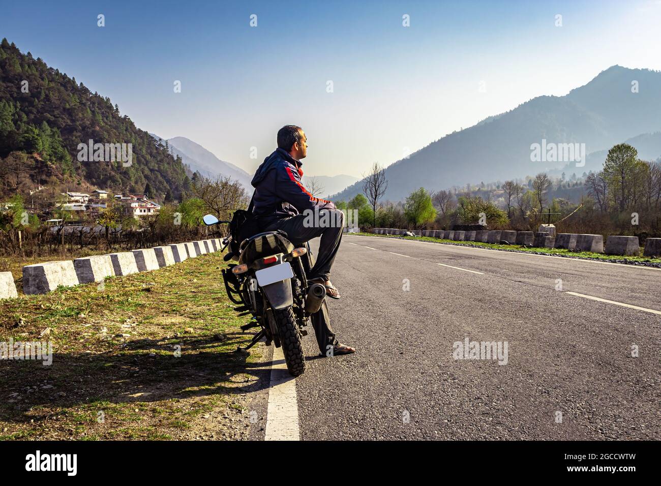 man sitting at motorcycle at tarmac road with beautiful natural view at morning image is taken at shergaon arunachal pradesh india. Stock Photo