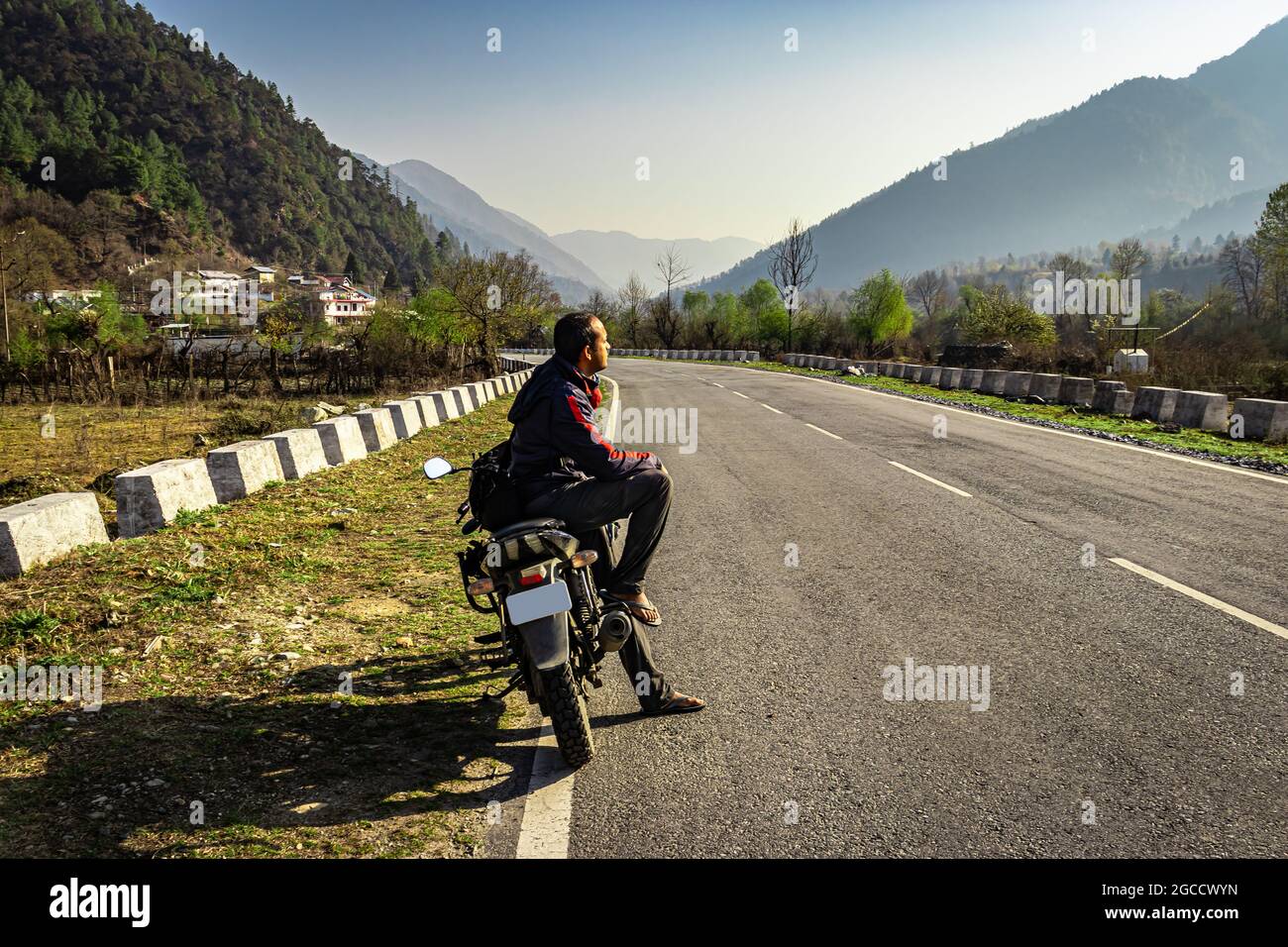 man sitting at motorcycle at tarmac road with beautiful natural view at morning image is taken at shergaon arunachal pradesh india. Stock Photo
