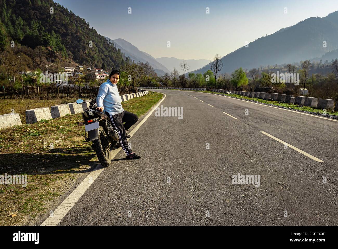 girl sitting at motorcycle at tarmac road with beautiful natural view at morning image is taken at shergaon arunachal pradesh india. Stock Photo