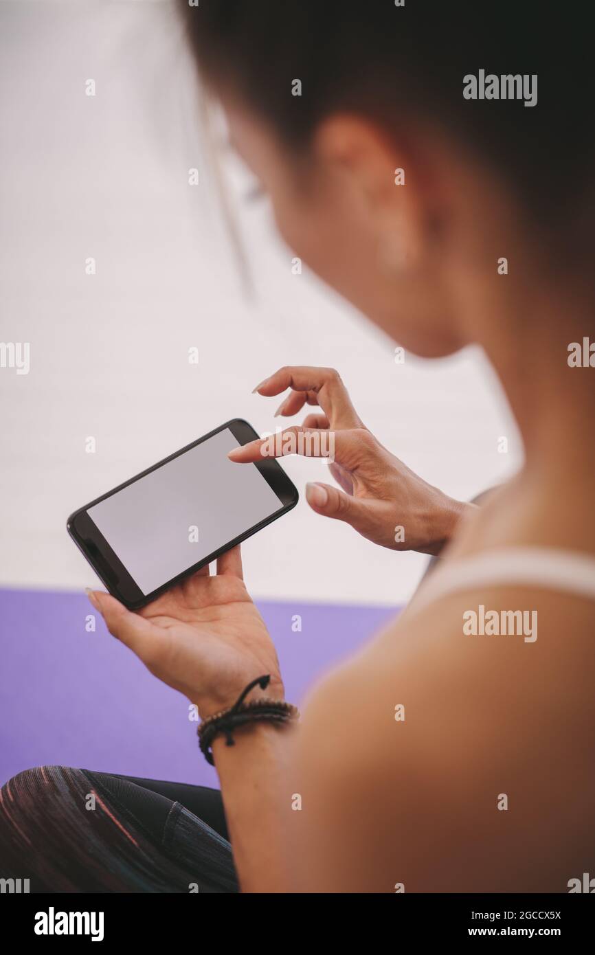 Closeup shot of woman using mobile phone at fitness studio. Woman using mobile phone after yoga exercise. Stock Photo