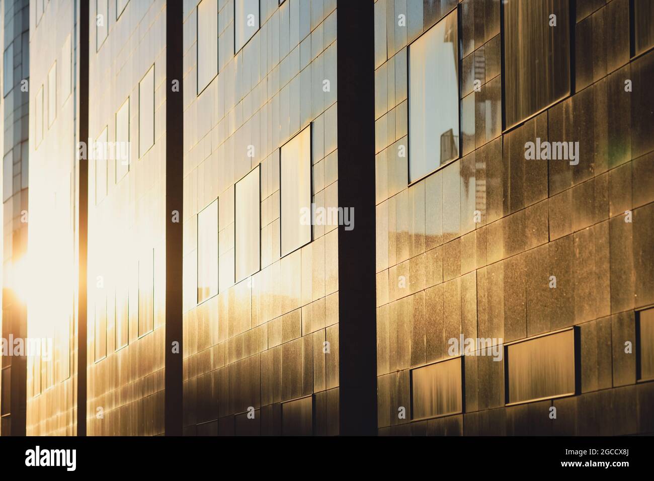 Setting sun is reflected in the windows of a tall glass office building ...