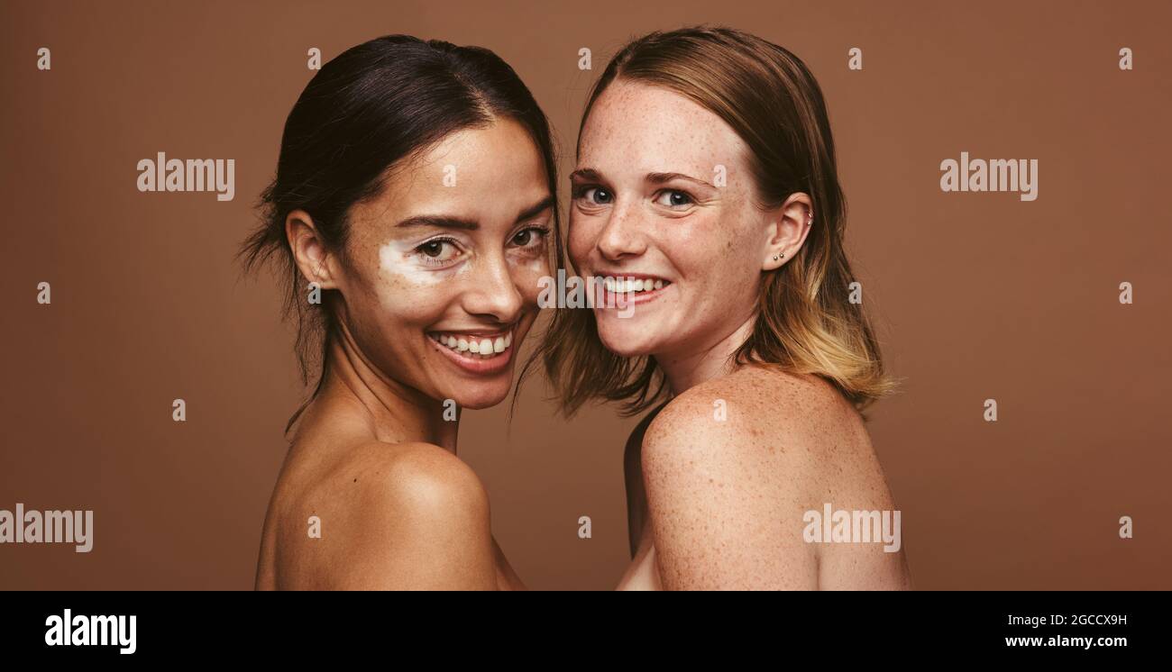 Close up of smiling young women with beautiful skin on brown background. Confident young women reflecting body positivity and self acceptance. Stock Photo