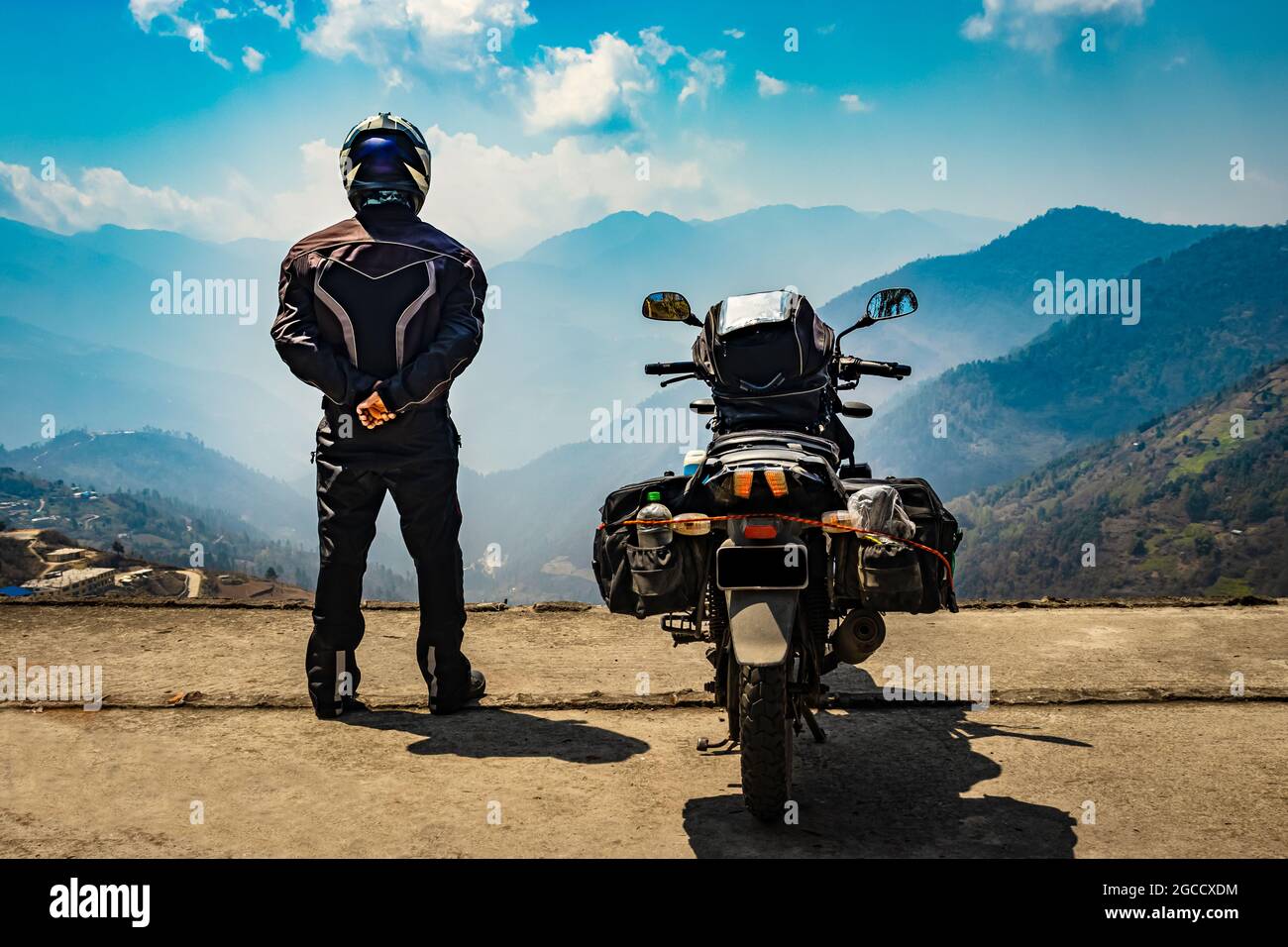 man motorcyclist standing at hill top with his loaded motorcycle and pristine natural view image is taken at bomdila arunachal pradesh india. Stock Photo