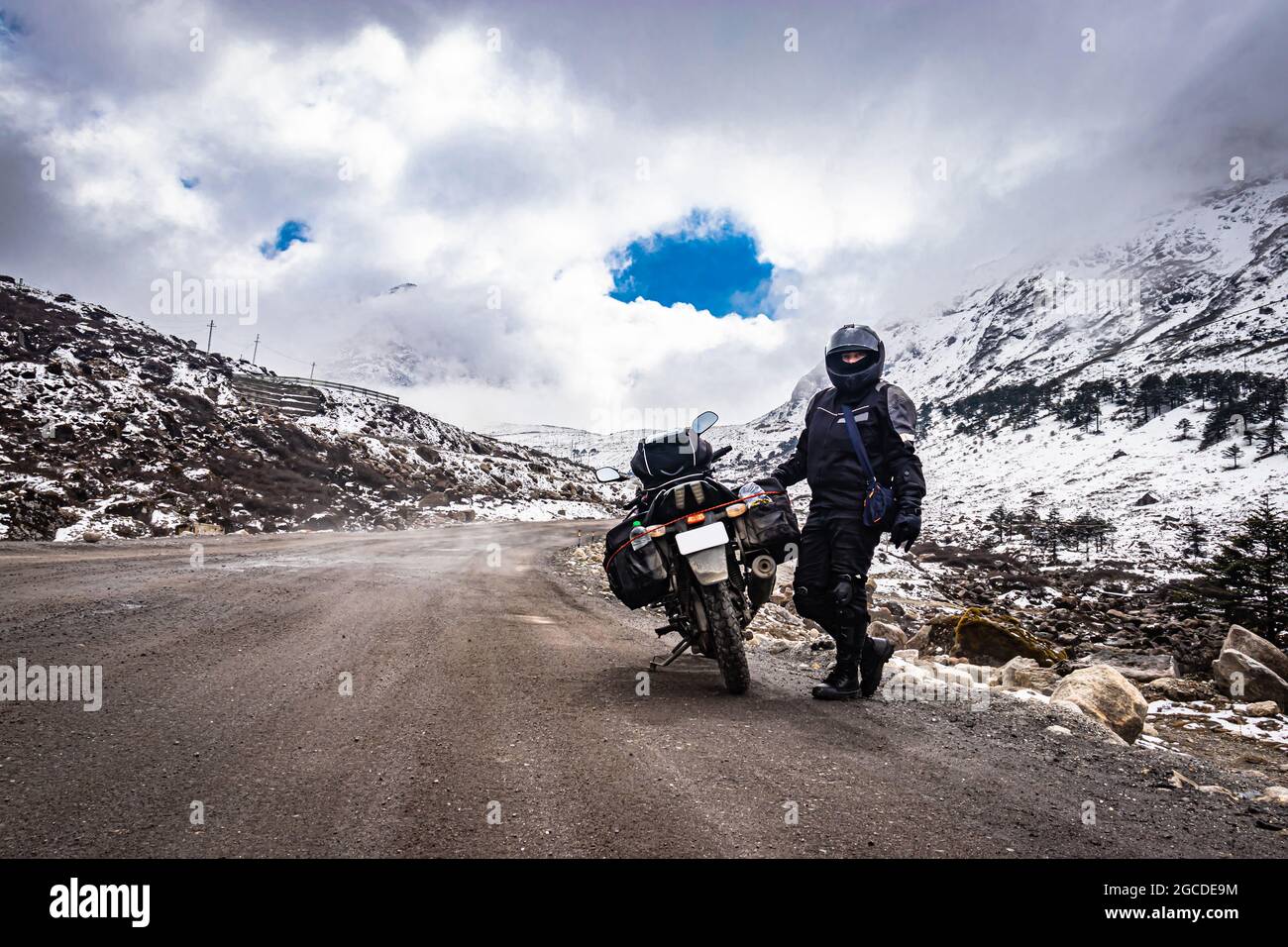 girl solo ridder in ridding gears with loaded motorcycle at isolated road and snow cap mountains image is taken at sela pass tawang arunachal pradesh. Stock Photo