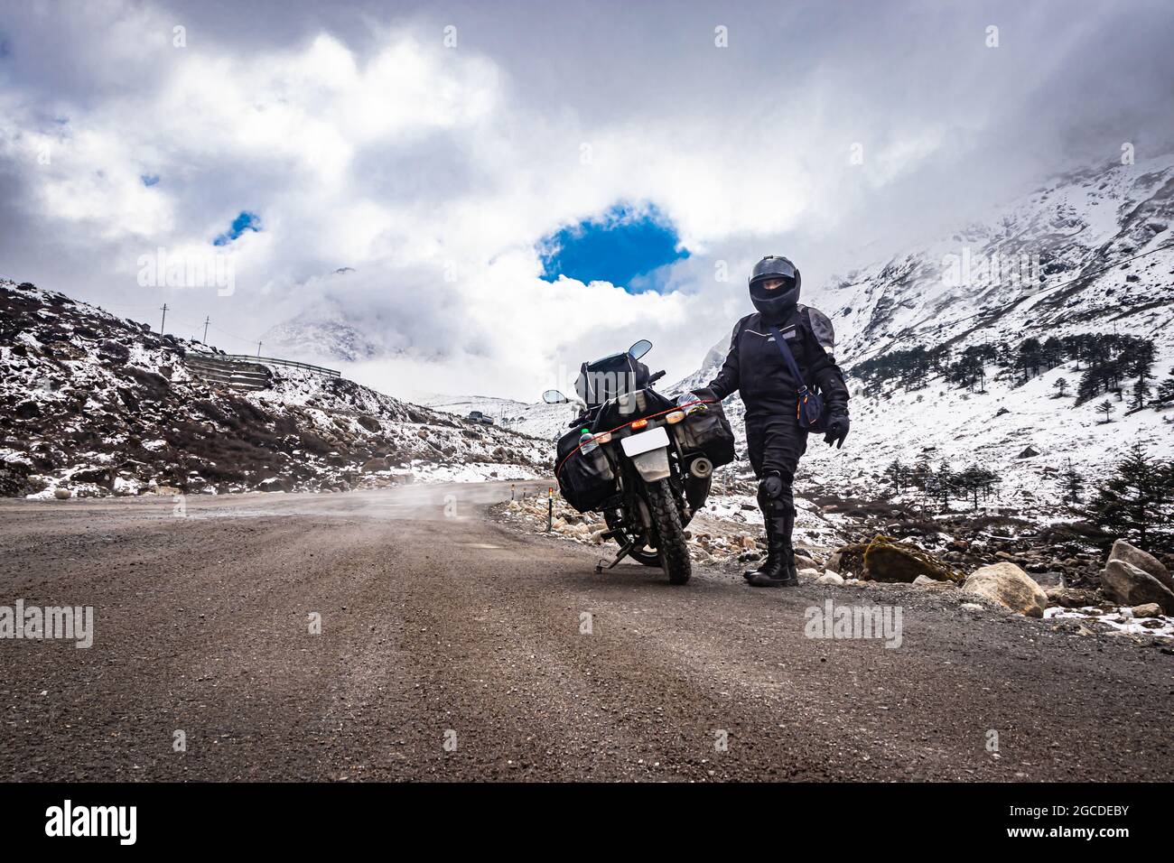 girl solo ridder in ridding gears with loaded motorcycle at isolated road and snow cap mountains image is taken at sela pass tawang arunachal pradesh. Stock Photo