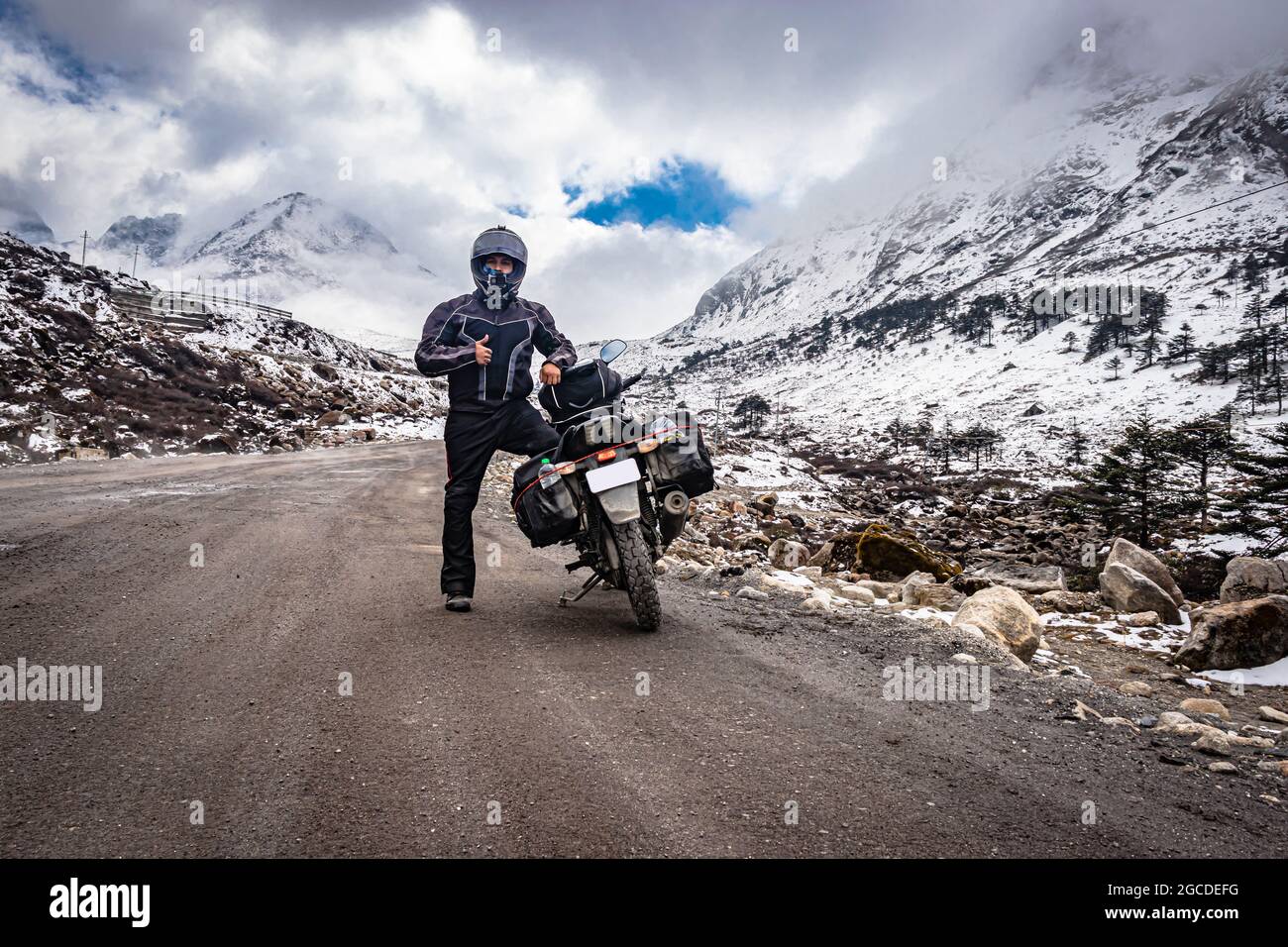 man solo ridder in ridding gears with loaded motorcycle at isolated road and snow cap mountains image is taken at sela pass tawang arunachal pradesh. Stock Photo