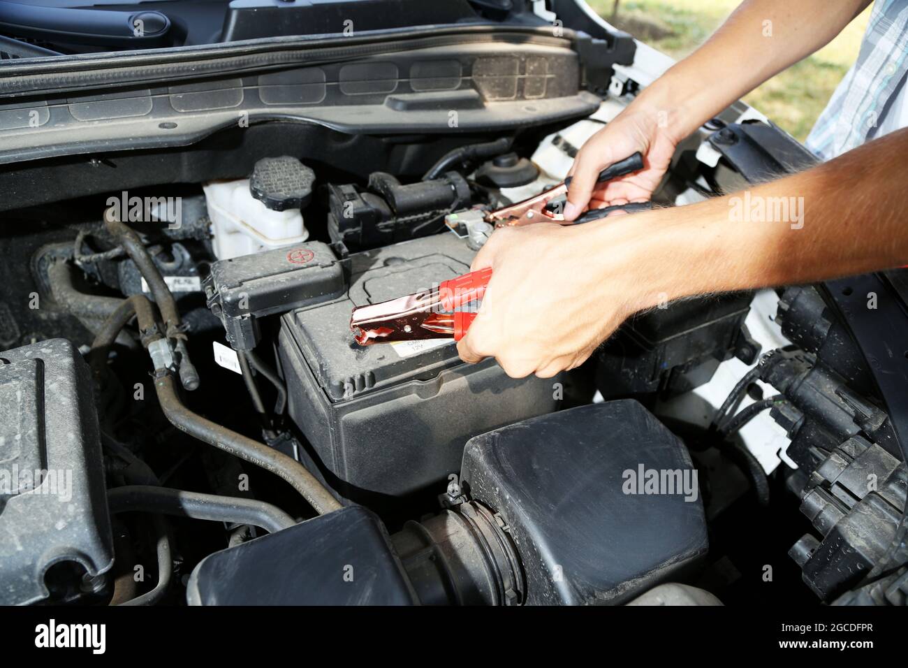 Car mechanic uses battery jumper cables to charge dead battery Stock