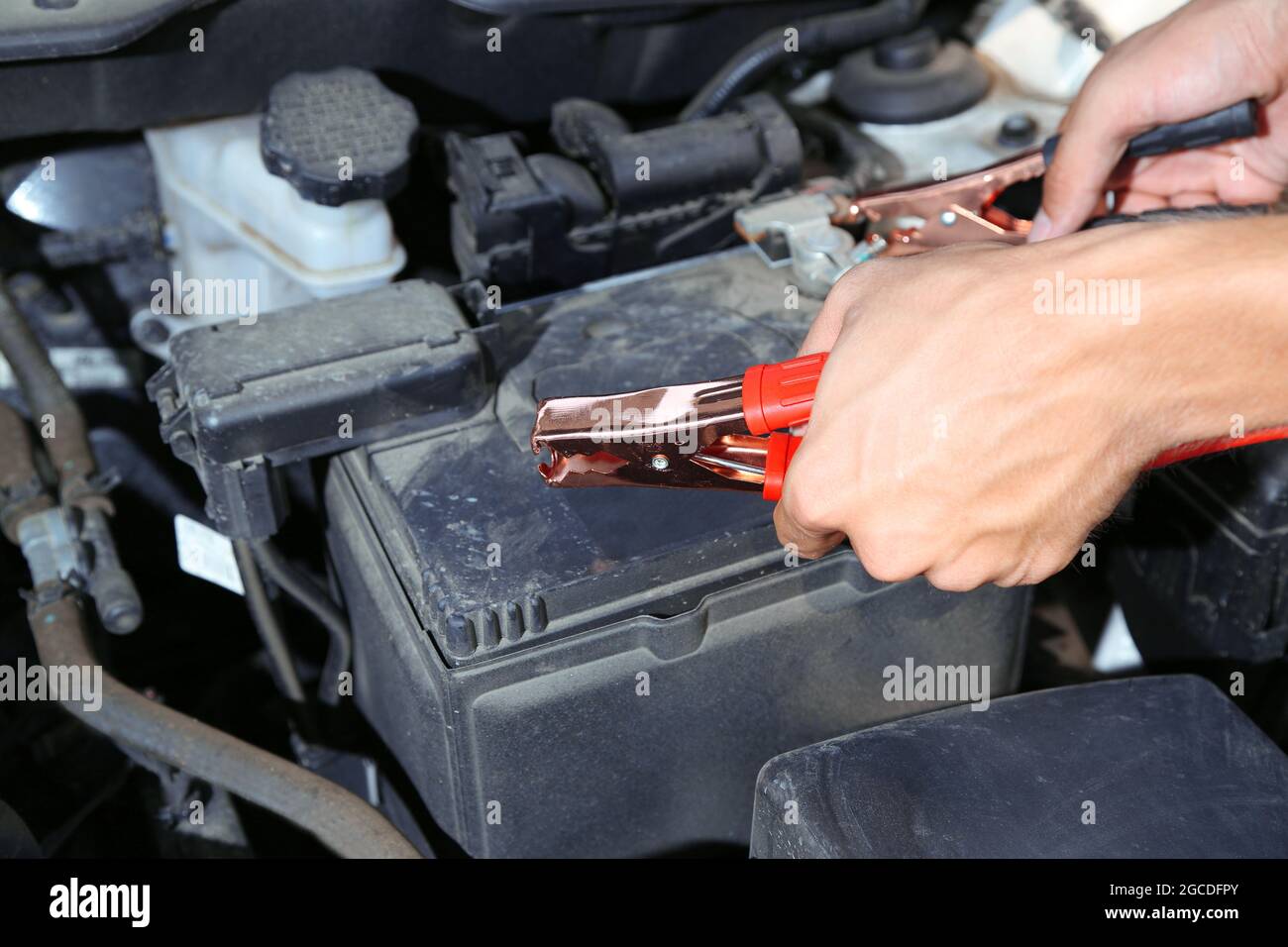 Car mechanic uses battery jumper cables to charge dead battery Stock