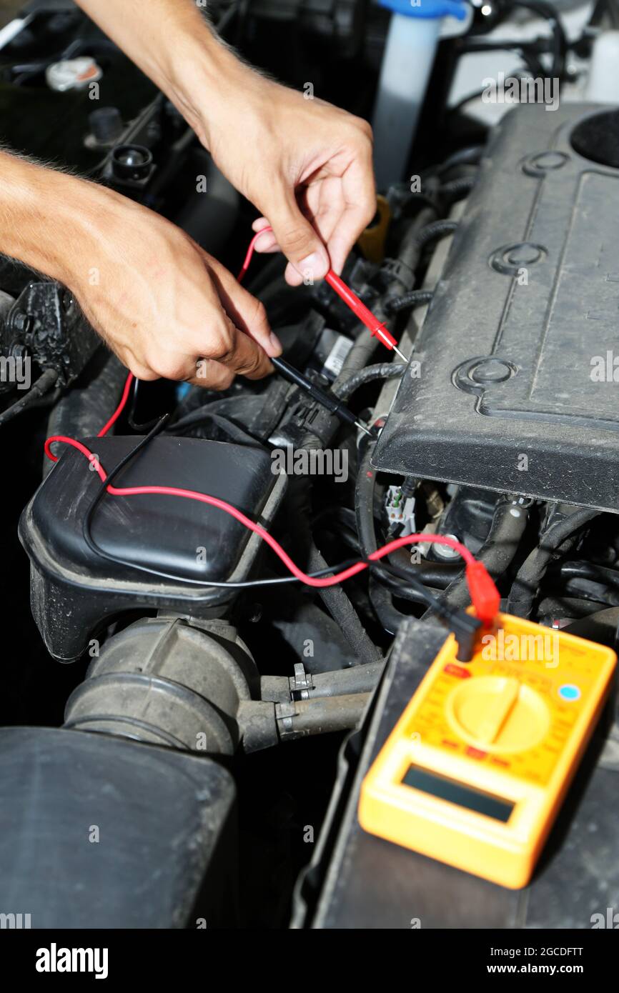 Auto mechanic uses multimeter voltmeter to check voltage level in car
