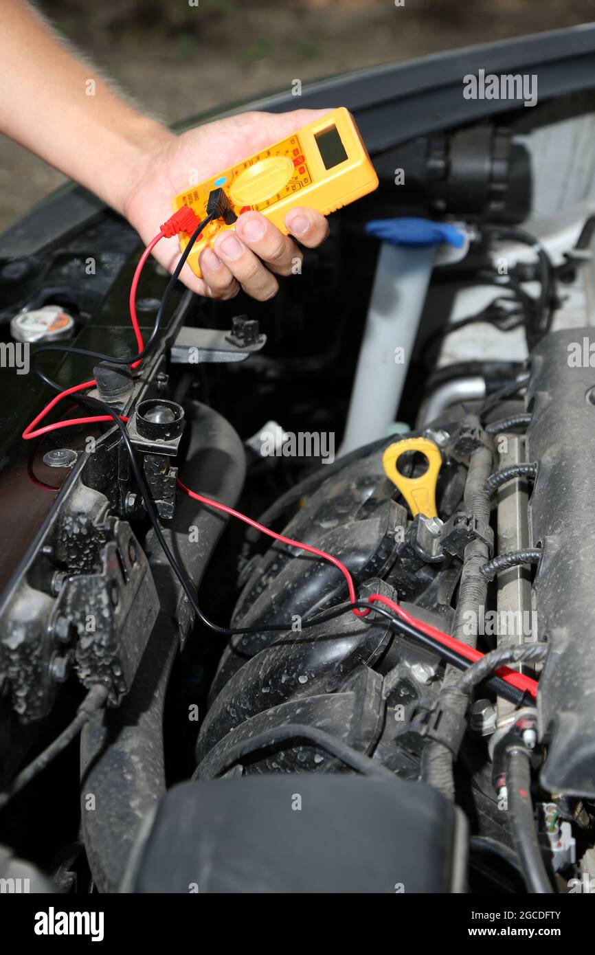 Auto mechanic uses multimeter voltmeter to check voltage level in car