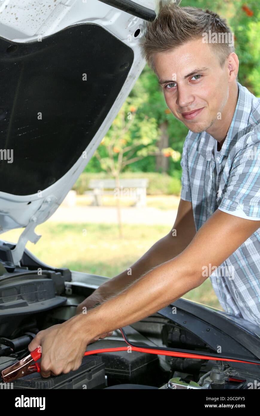 Young driver uses battery jumper cables to charge dead battery Stock
