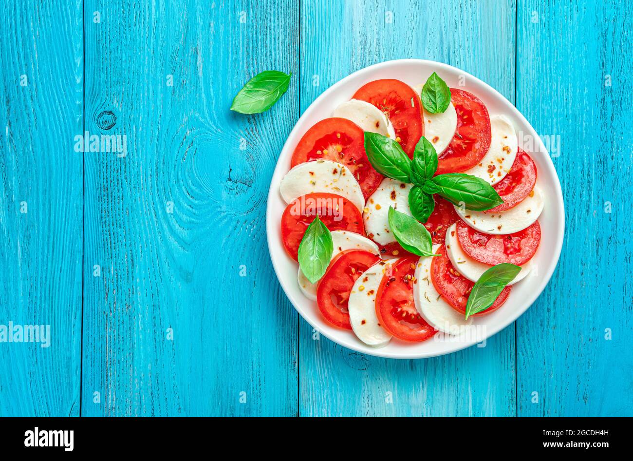 Caprese salad with fresh tomatoes, mozzarella cheese and basil leaves on a blue background. Stock Photo