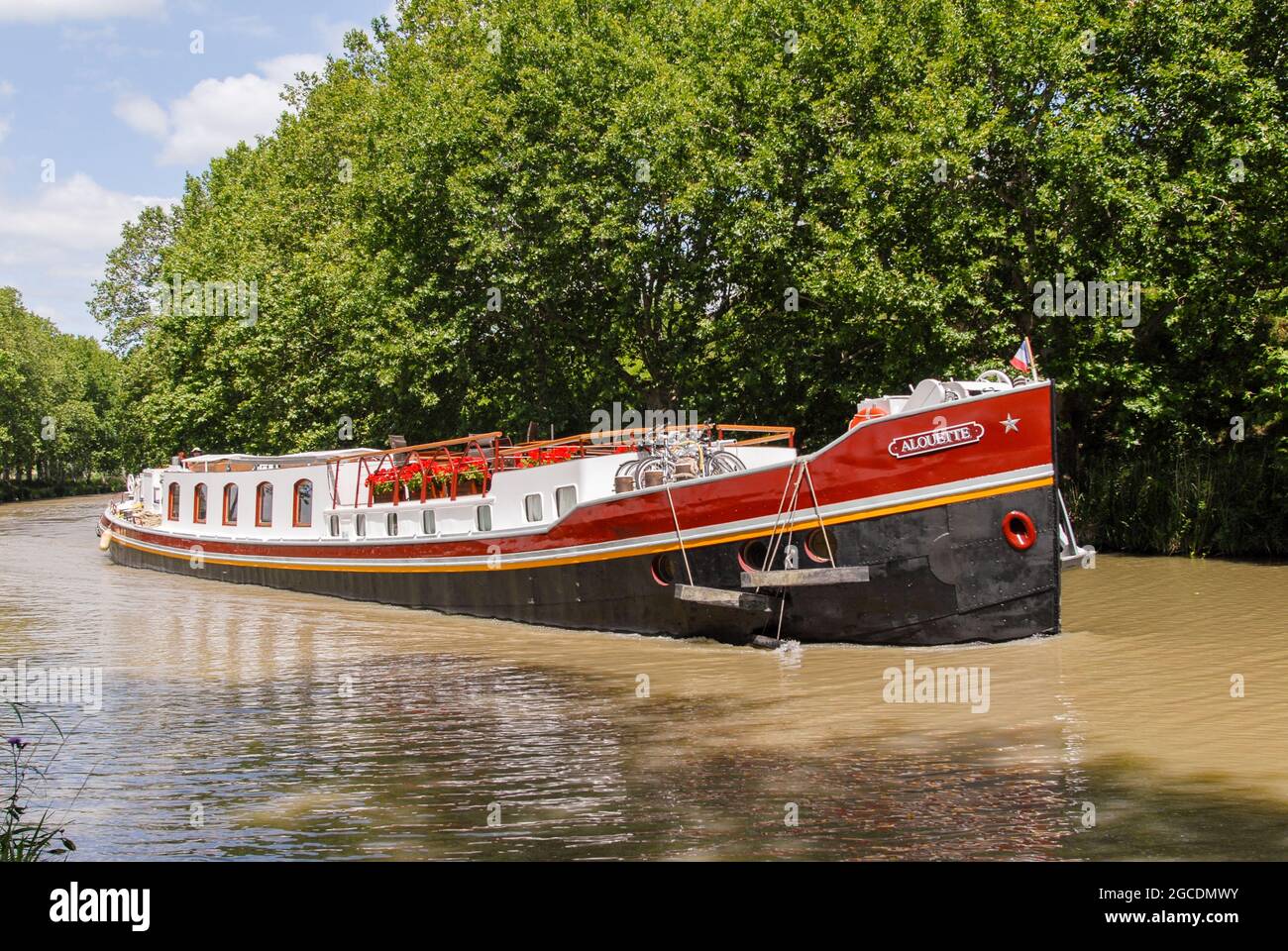 A former barge used as a houseboat navigates on the Canal du Midi Stock Photo