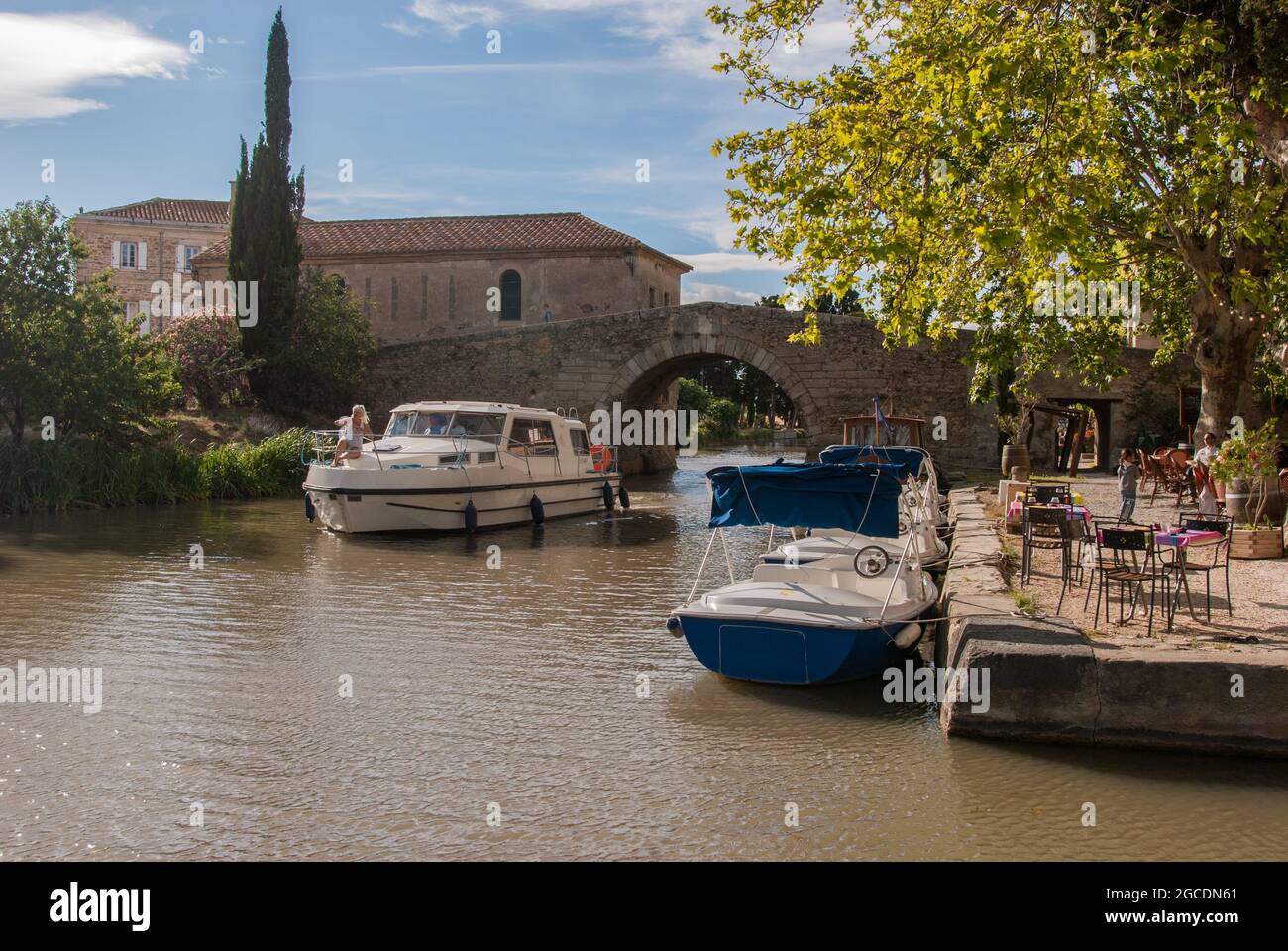 A boat on the Canal du Midi crossing under the old bridge of Somail. Stock Photo