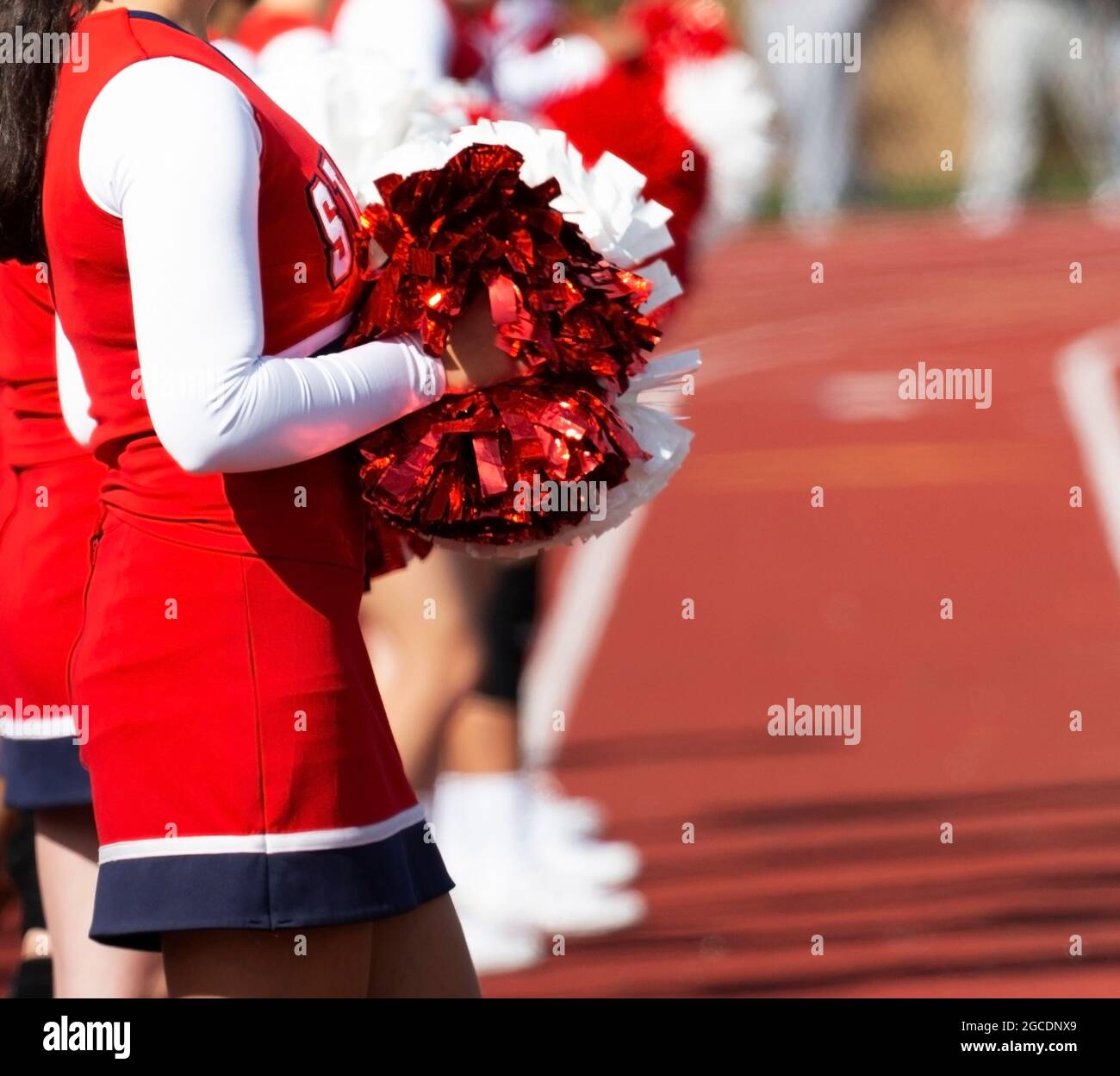 High school cheerleaders standing on a red track holding their pom poms in front of them. Stock Photo