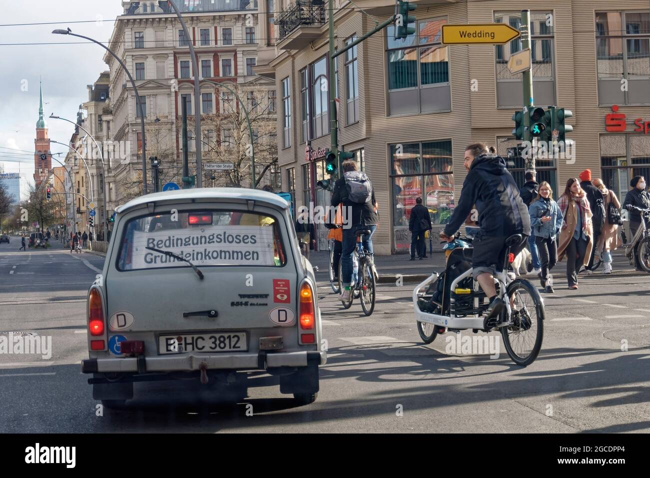 Trabi mit Schild  ' Bedingungsloses Grundeinkommen ' , Fahrradfahrer , Eberswalder Ecke Schoenhauser Allee Prenzlauer Berg, Berlin Stock Photo