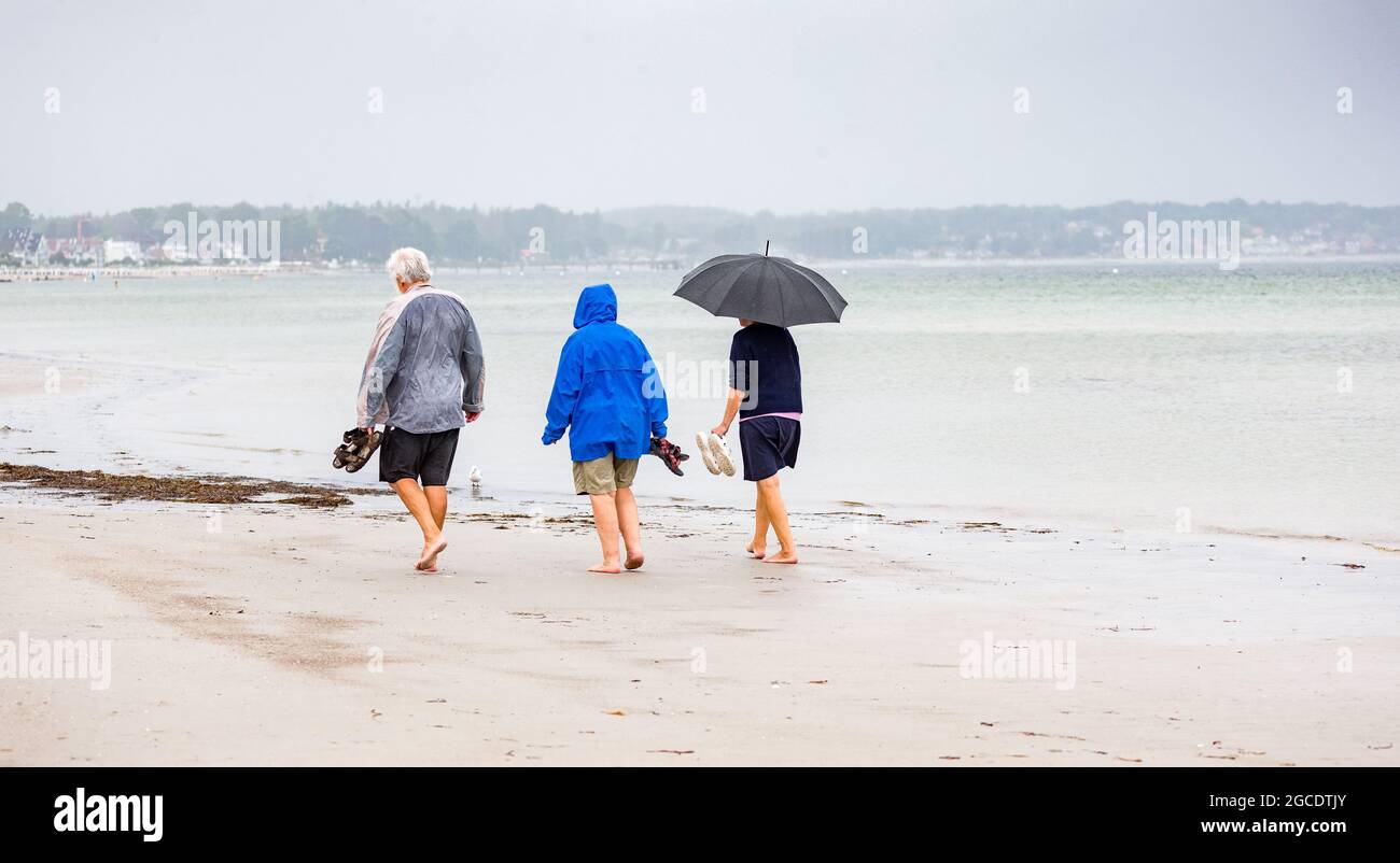 Scharbeutz, Germany. 08th Aug, 2021. Three walkers in rain jackets and